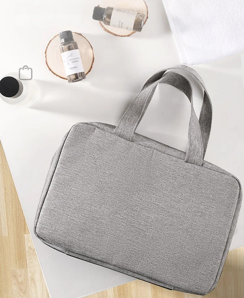 Trousse de toilette de voyage fermée en tissu gris, format compact avec poignée, facile à transporter dans une valise ou un sac de voyage.